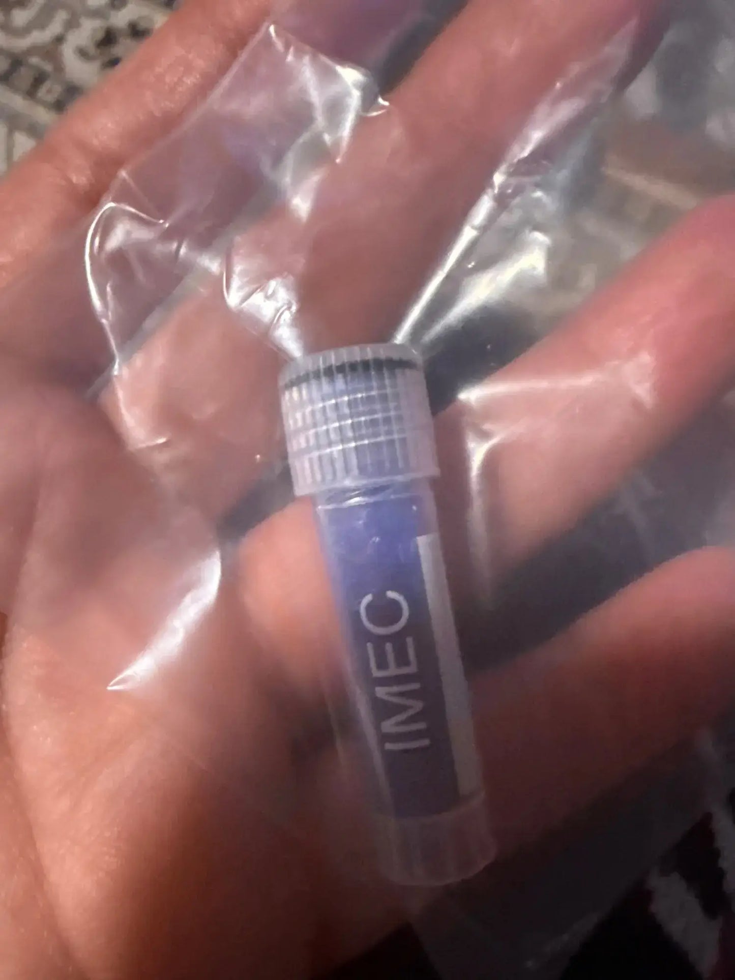 Close-up of a hand holding an IMEC vial in a sealed bag, showcasing its sleek design.